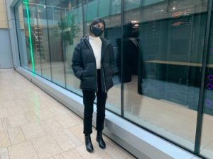 Saamin is wearing a black mask and standing next to a glass wall through which large computer servers can be seen